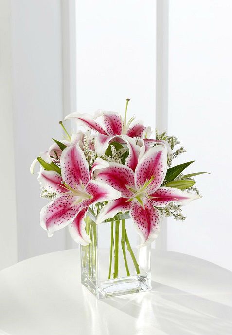 a vase filled with pink and white lilies on top of a table next to a window