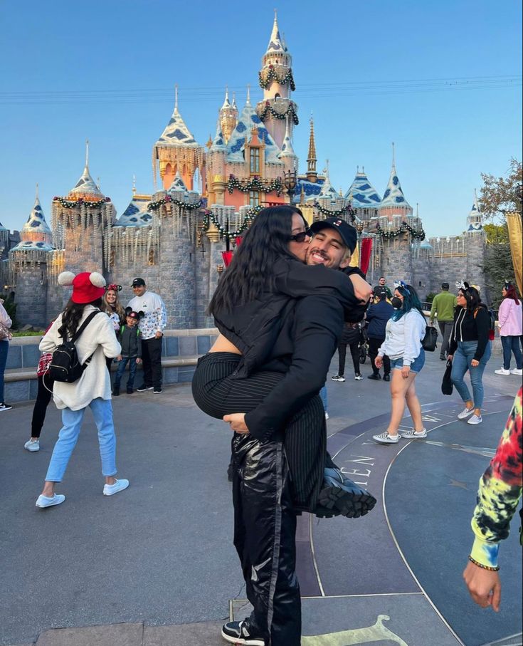 two people hugging each other in front of a castle with lots of people walking around