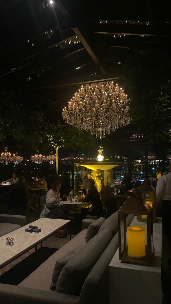 people sitting at tables in a restaurant with chandeliers hanging from the ceiling