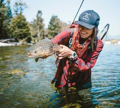 a woman is holding a fish in the water while wearing a hat and fishing gear