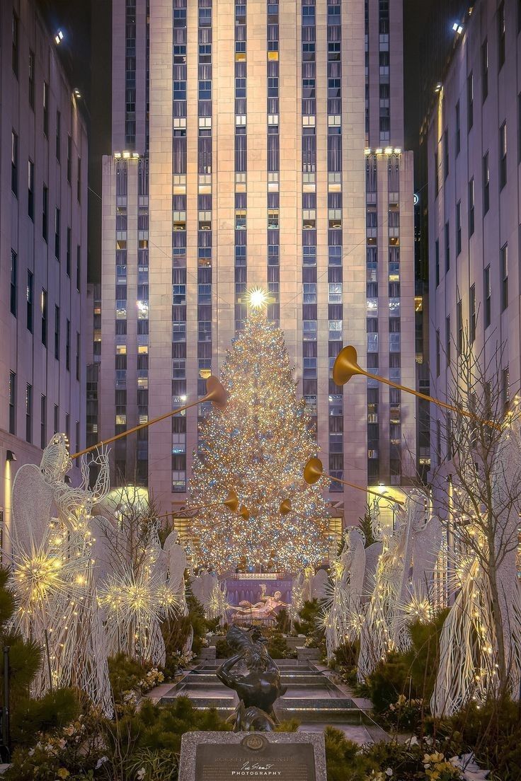 the christmas tree is surrounded by angel statues in front of tall buildings with lights on them