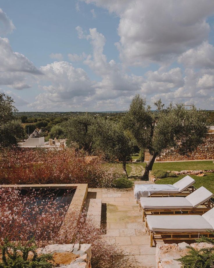 an outdoor pool with lounge chairs and olive trees in the background, surrounded by stone walls