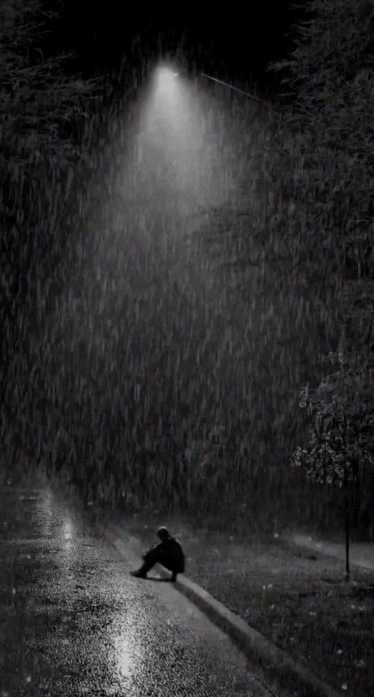 a person kneeling down in the rain at night with an umbrella and street light above them