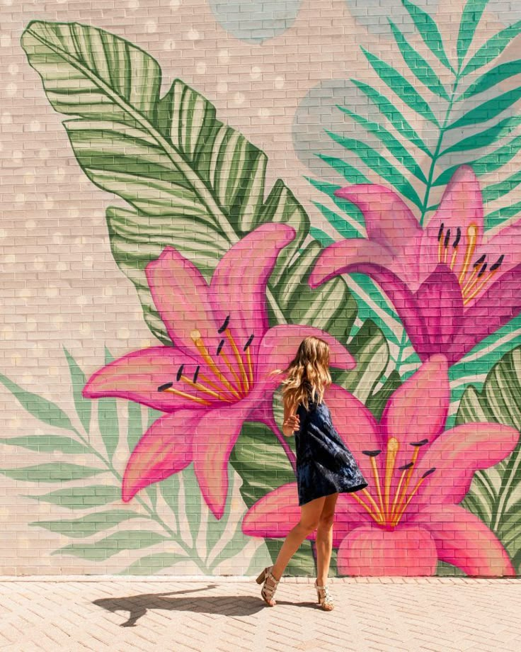 a woman standing in front of a wall with pink flowers painted on it and palm leaves