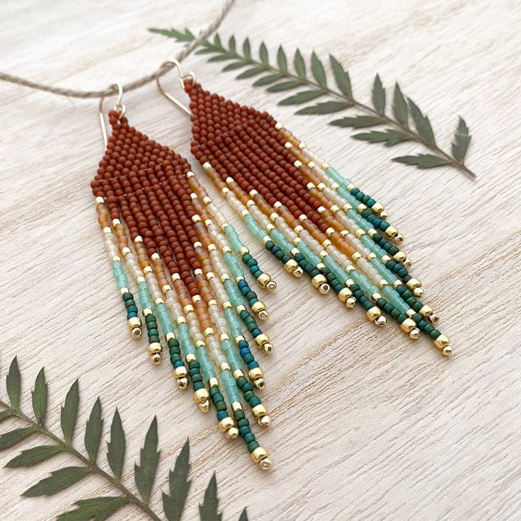 the beaded earrings are hanging from a string on a wooden table with green leaves