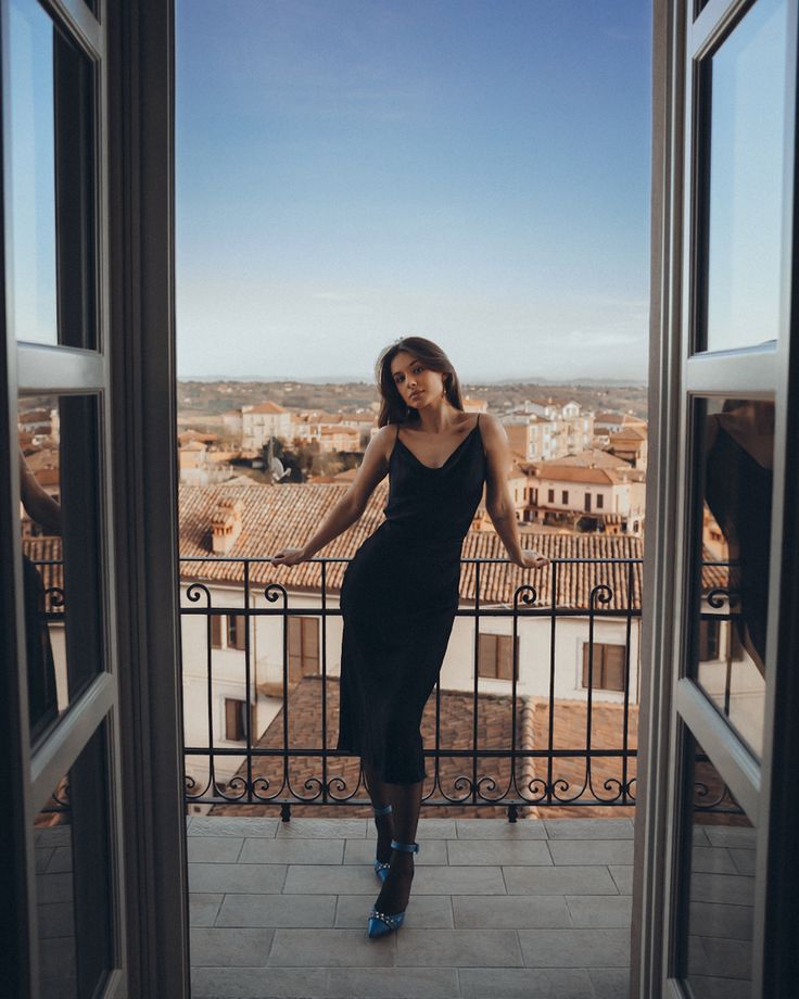 a woman standing on top of a balcony next to an open door with the city in the background