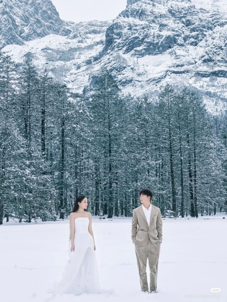 a bride and groom standing in the snow with mountains in the background