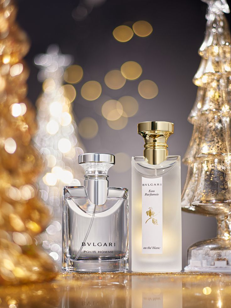 two perfume bottles sitting on top of a table next to a christmas tree with lights in the background