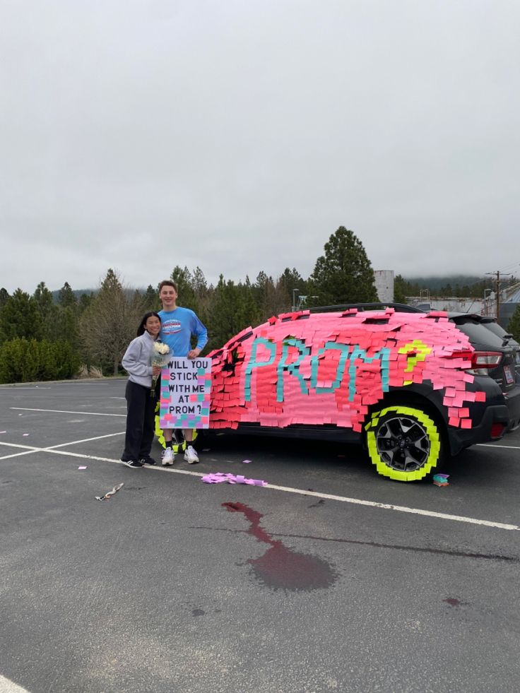 a man and woman standing next to a car made out of legos in a parking lot