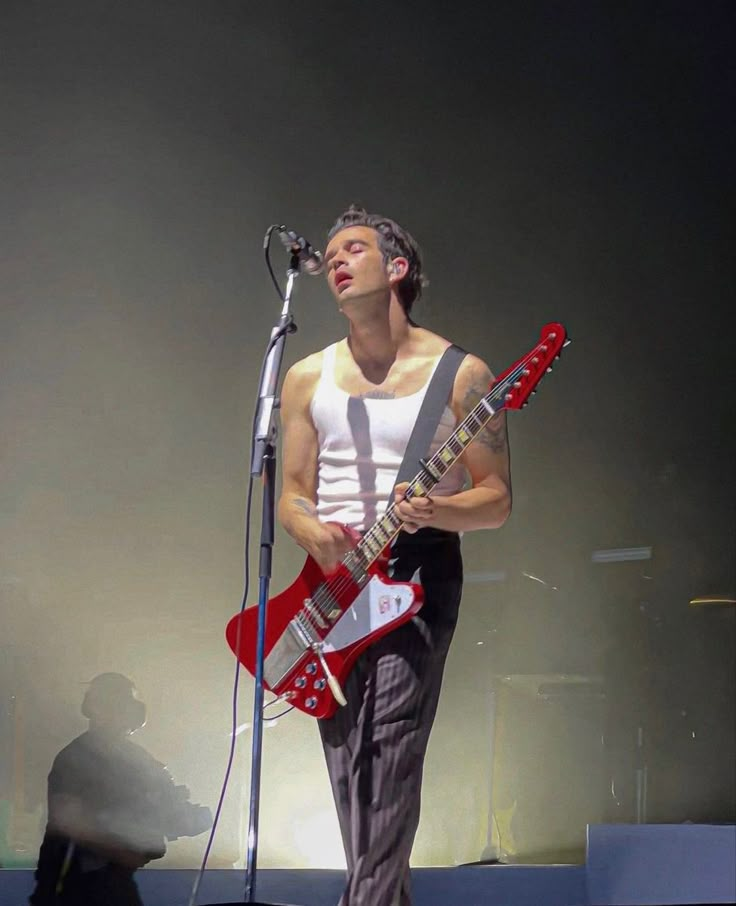 a young man holding a guitar while standing in front of a microphone