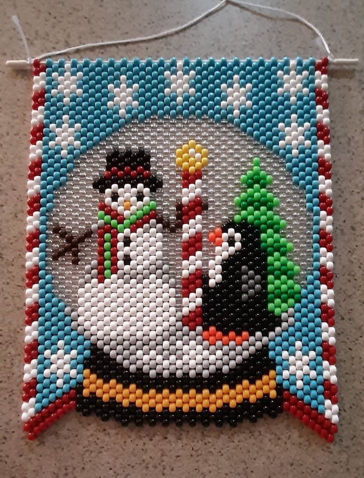 a beaded christmas ornament hanging on a wall with snowmen in the background