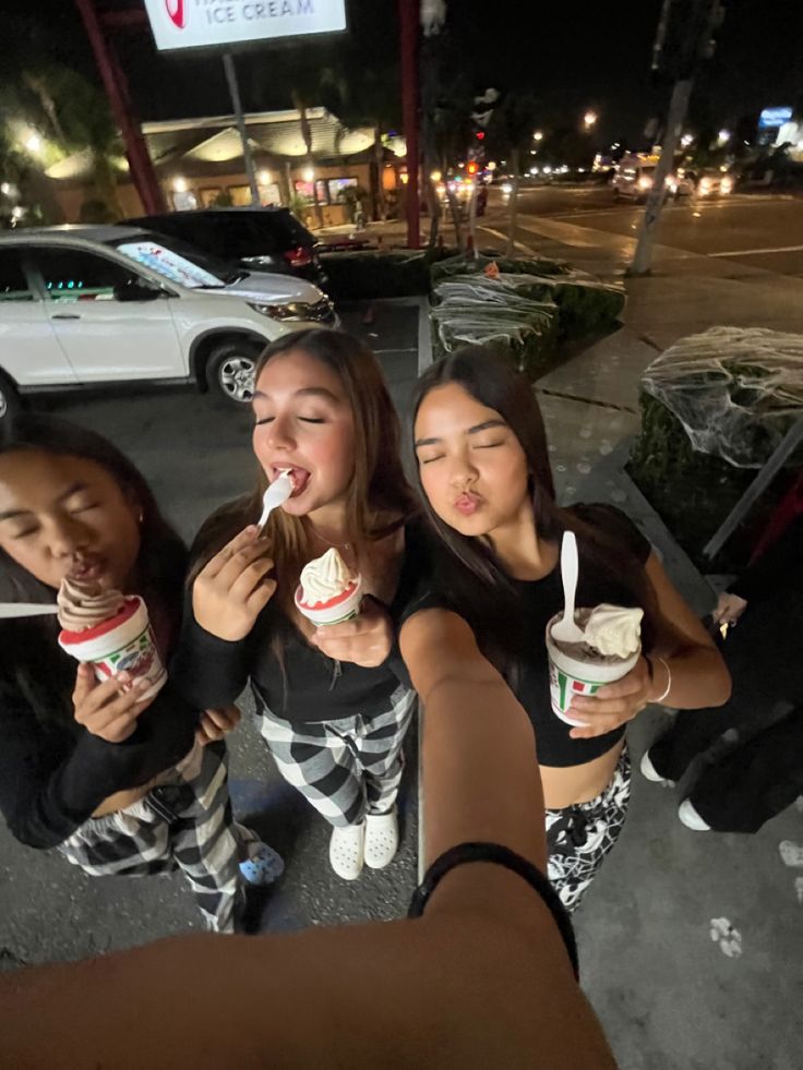 three girls eating ice cream at night on the sidewalk