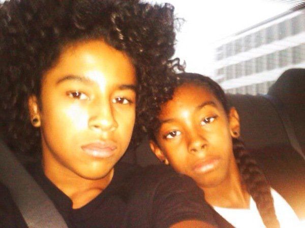 two young people sitting in the back seat of a car, one with curly hair