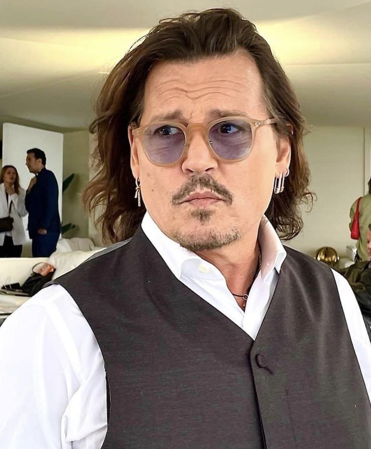 a man with long hair wearing sunglasses and a vest