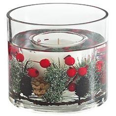 a clear glass candle holder with red flowers and pine cones on the inside is filled with water