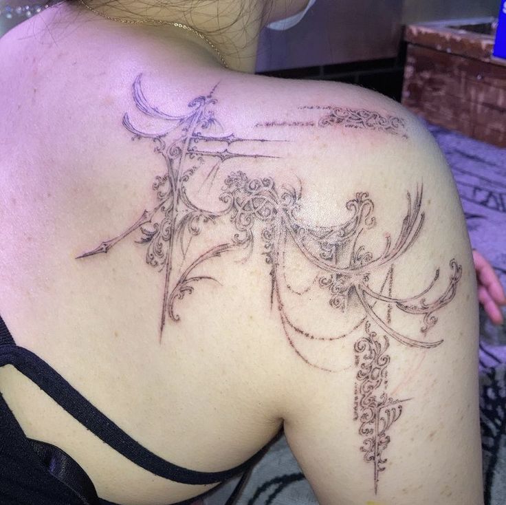 the back of a woman's shoulder with an intricate tattoo design on her upper arm