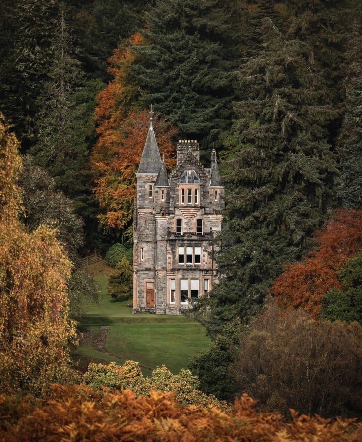 an old building in the middle of some trees with fall foliage around it and leaves on the ground