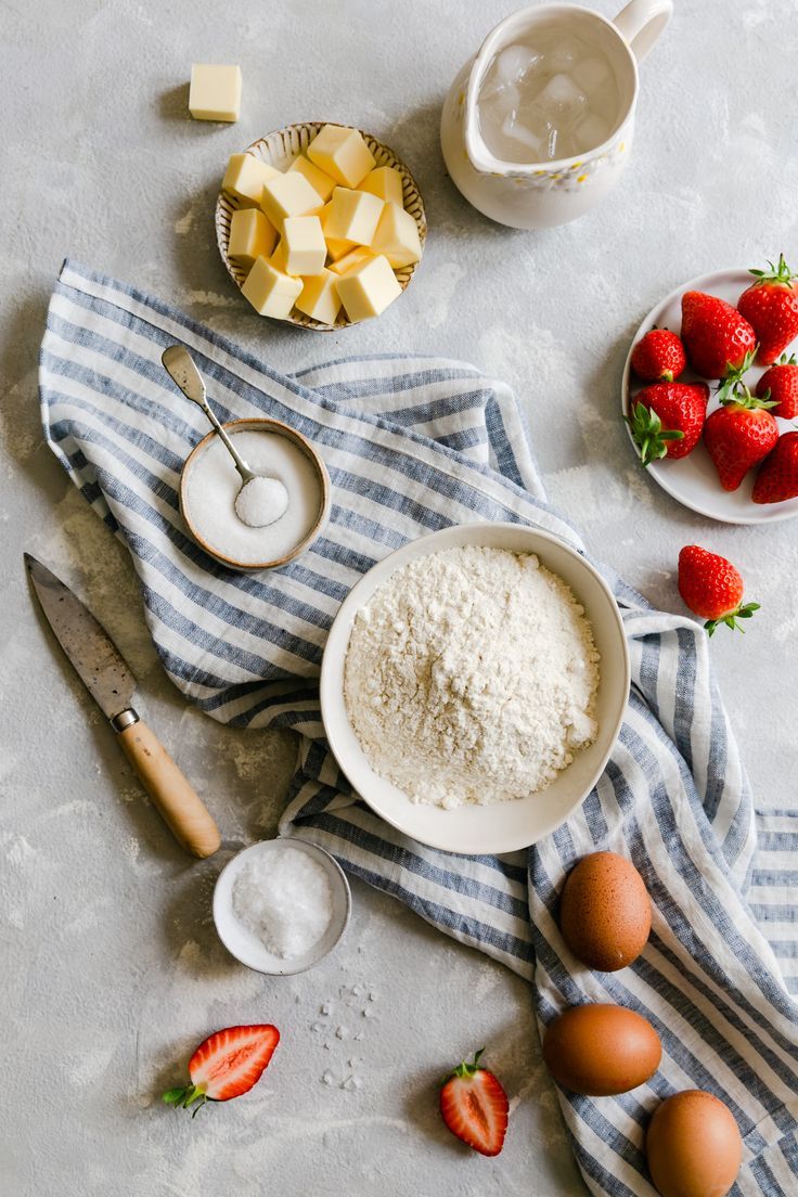 ingredients to make strawberry shortcakes laid out on a white tablecloth with blue and white striped towel