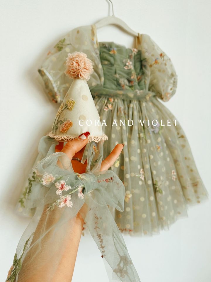 a hand holding a doll wearing a dress and a party hat with flowers on it