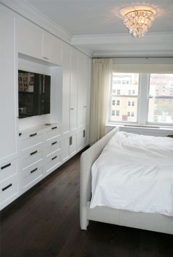 a white bed sitting in a bedroom next to a tv on top of a dresser