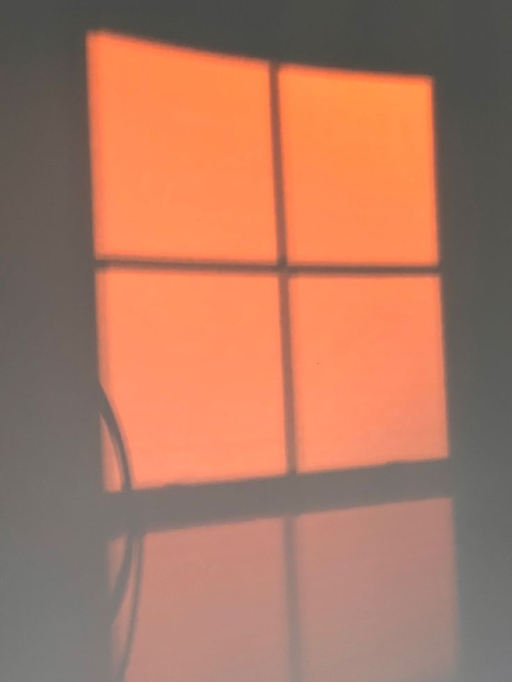 the shadow of a chair is cast on a wall by a window with an orange light coming through it