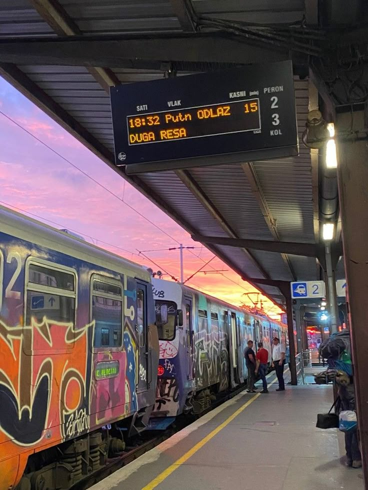 a train with graffiti painted on the side is at a station as people wait to board