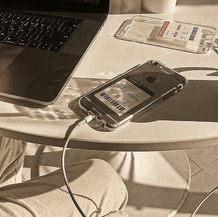 a cell phone plugged into a charger on a table next to a laptop