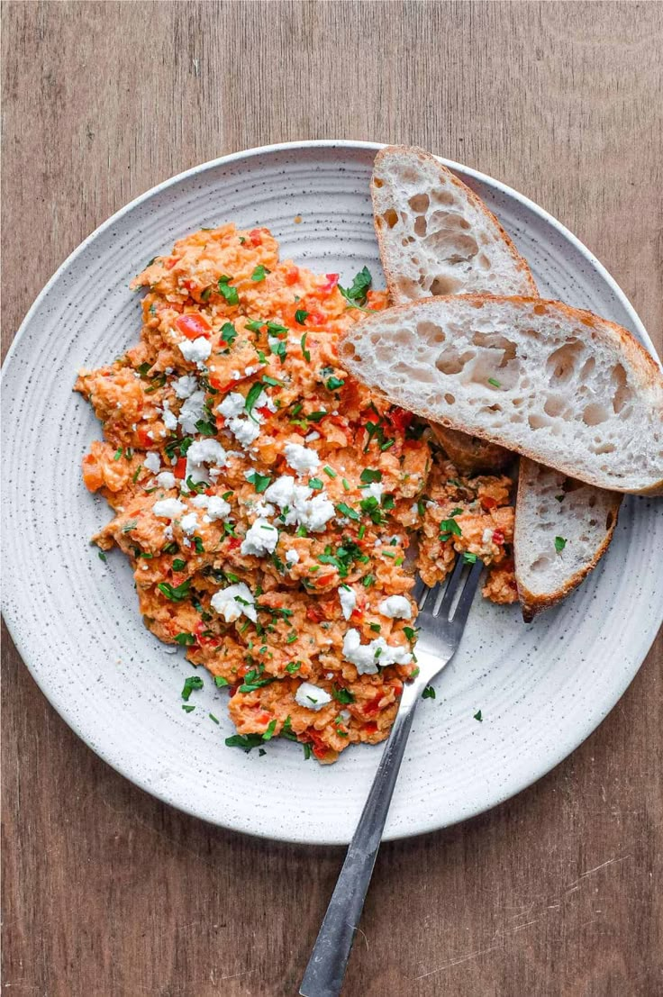 a white plate topped with eggs and bread on top of a wooden table next to a fork