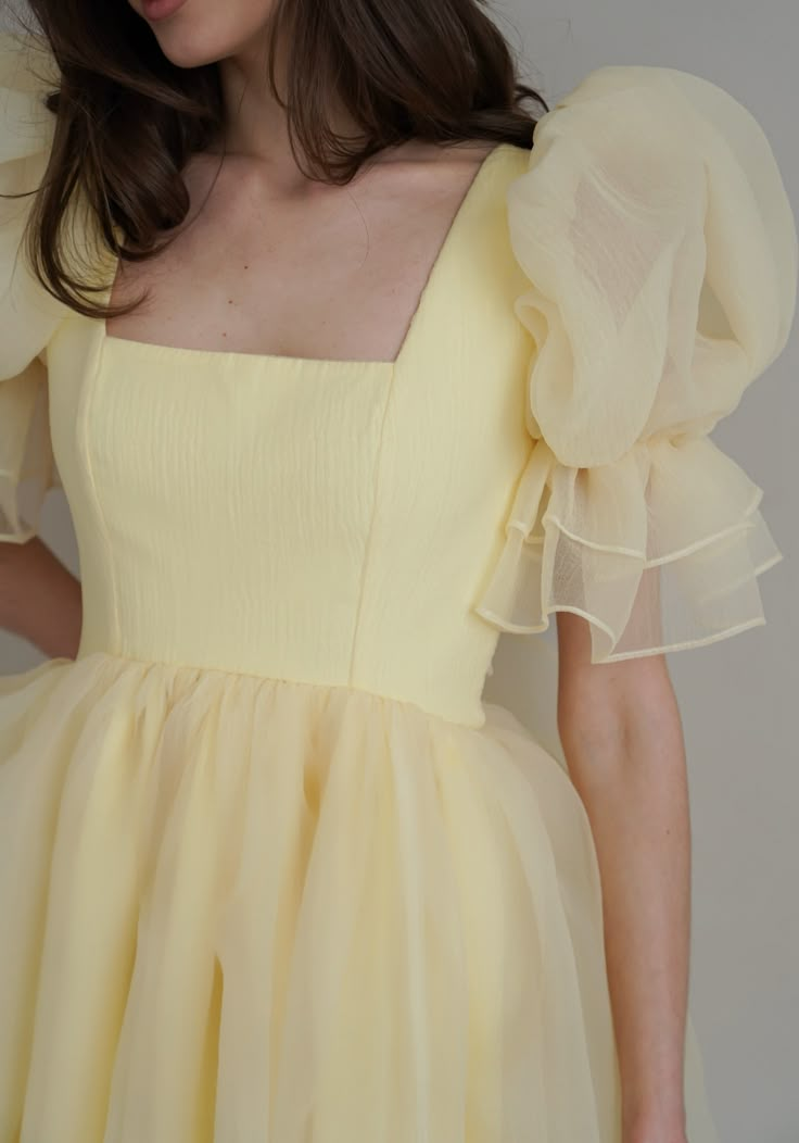 Introducing the Britney Dress in a delightful light yellow: a stunning creation crafted from delicate bubble organza. This lightweight dress features an elegant silhouette with a voluminous floating skirt that moves gracefully with every step. The charming puff sleeves add a whimsical touch, making it perfect for any special occasion. The Britney Dress is enclosed with delicate bow ties down the back, adding a romantic and feminine detail that completes the look. In light yellow, this dress exud Yellow Dress Puffy Sleeves, Ruffles Sleeves Dress, Womens Frocks Design, Ballet Inspired Dress, Sleeves Design For Frocks, Marriage Function Dresses For Women, Organza Dress Styles, Organza Sleeves Design, Yellow Dress With Sleeves