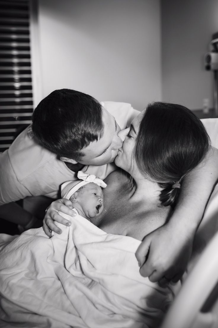 a man and woman kissing while holding a baby in their arms on a hospital bed