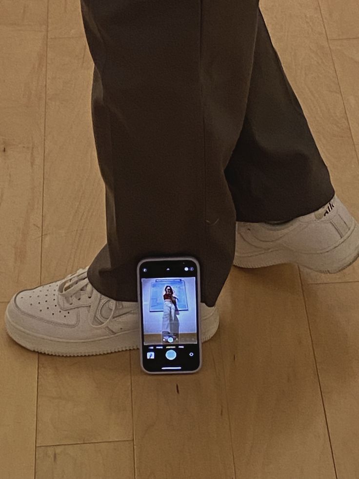 a person standing on a wooden floor holding a cell phone in their right hand and an image of a woman's feet