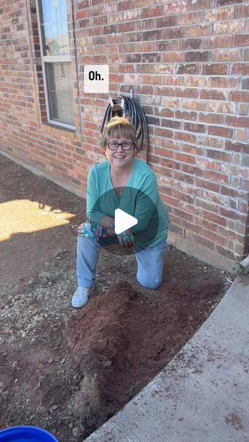 a woman kneeling on the ground next to a brick building with a hole in it