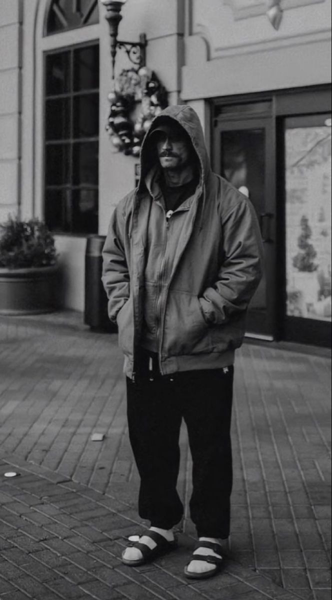 a man standing on the sidewalk in front of a building wearing a jacket and slippers