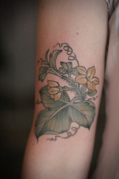 a close up of a person's arm with flowers and leaves tattooed on it