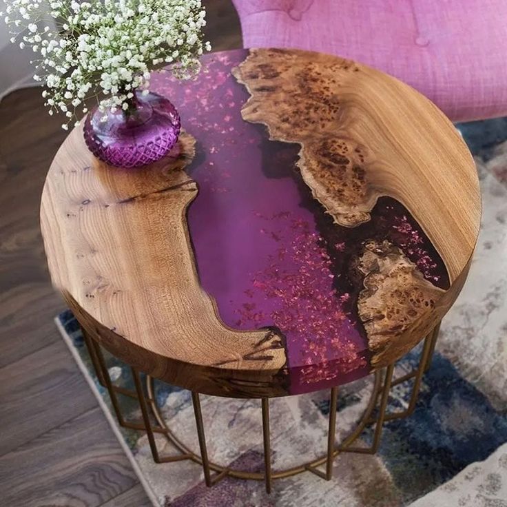 a wooden table with purple paint on it next to a pink chair and flower vase