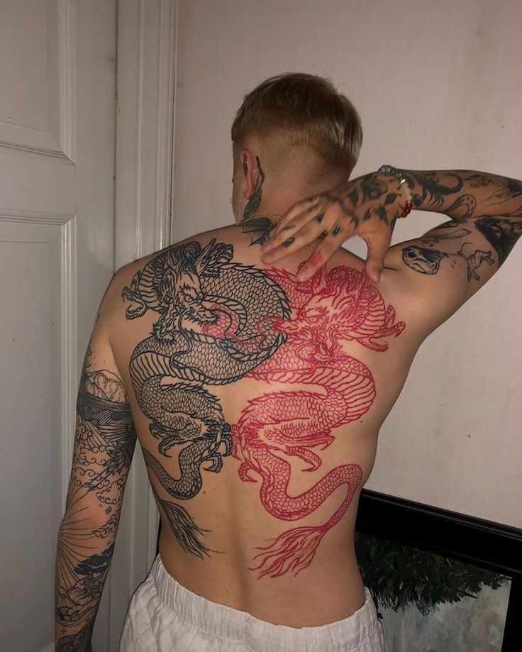 a man with dragon tattoos on his back and arms, standing in front of a door