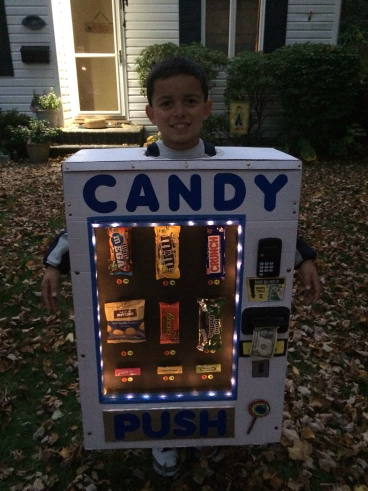 a young boy is dressed up as a candy vending machine in front of a house