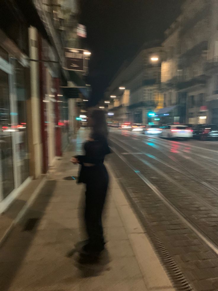 a blurry photo of a person walking down the street at night with buildings in the background