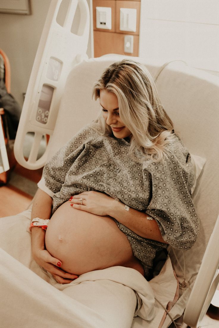 a pregnant woman sitting in a hospital bed with her stomach wrapped around her waist and looking down