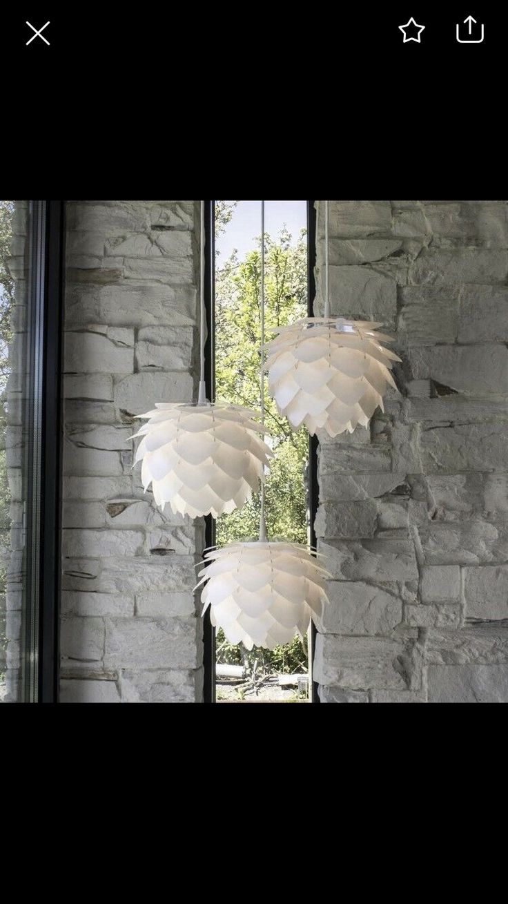 three lamps hanging from the ceiling in front of a stone wall with windows and grass