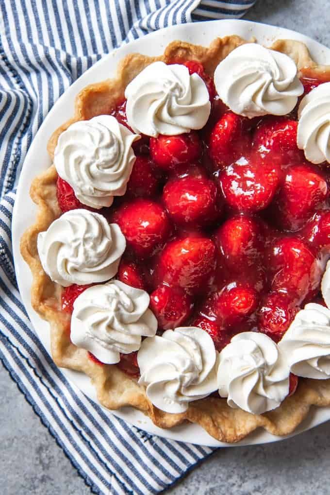 a pie topped with whipped cream and strawberries on a blue and white striped cloth