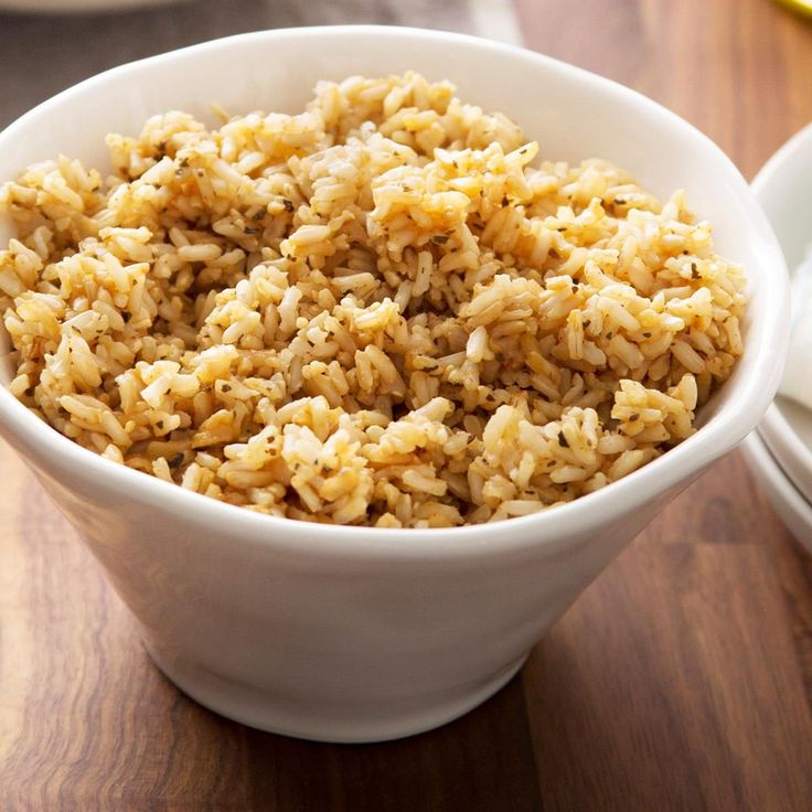 a white bowl filled with rice on top of a wooden table next to plates and utensils