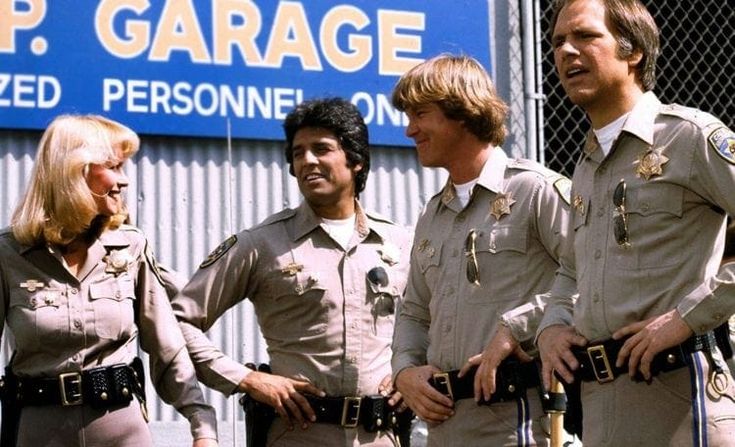 three police officers standing in front of a garage sign talking to two women and one man