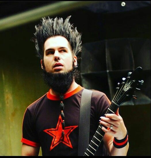 a man with black hair holding a guitar in his right hand and wearing a red star t - shirt