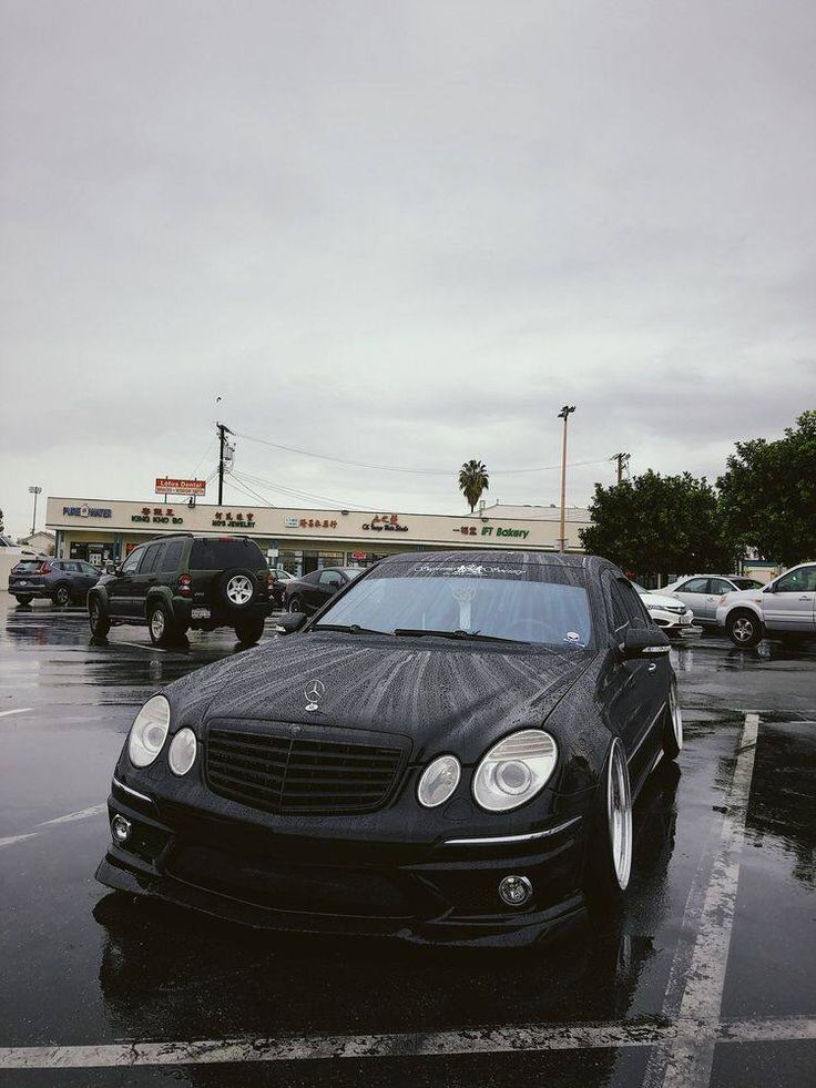 a black mercedes parked in a parking lot on a rainy day with cars behind it