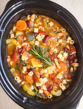 a black crock pot filled with soup and vegetables on top of a wooden table