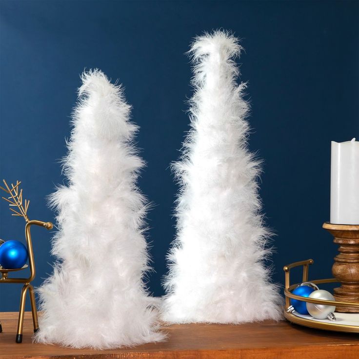 two tall white feather candlesticks sitting on top of a wooden table next to a candle