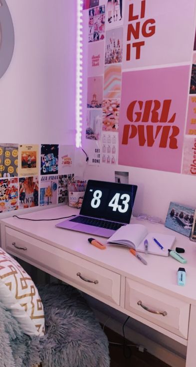 a white desk topped with a laptop computer sitting next to a wall covered in pictures