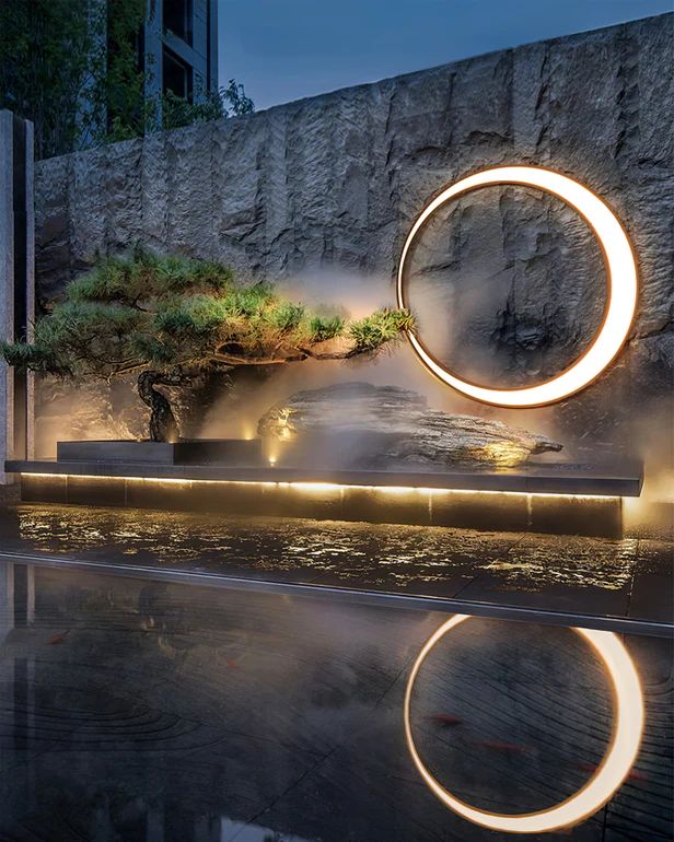 an artistic sculpture is lit up in front of a wall and reflecting water at night