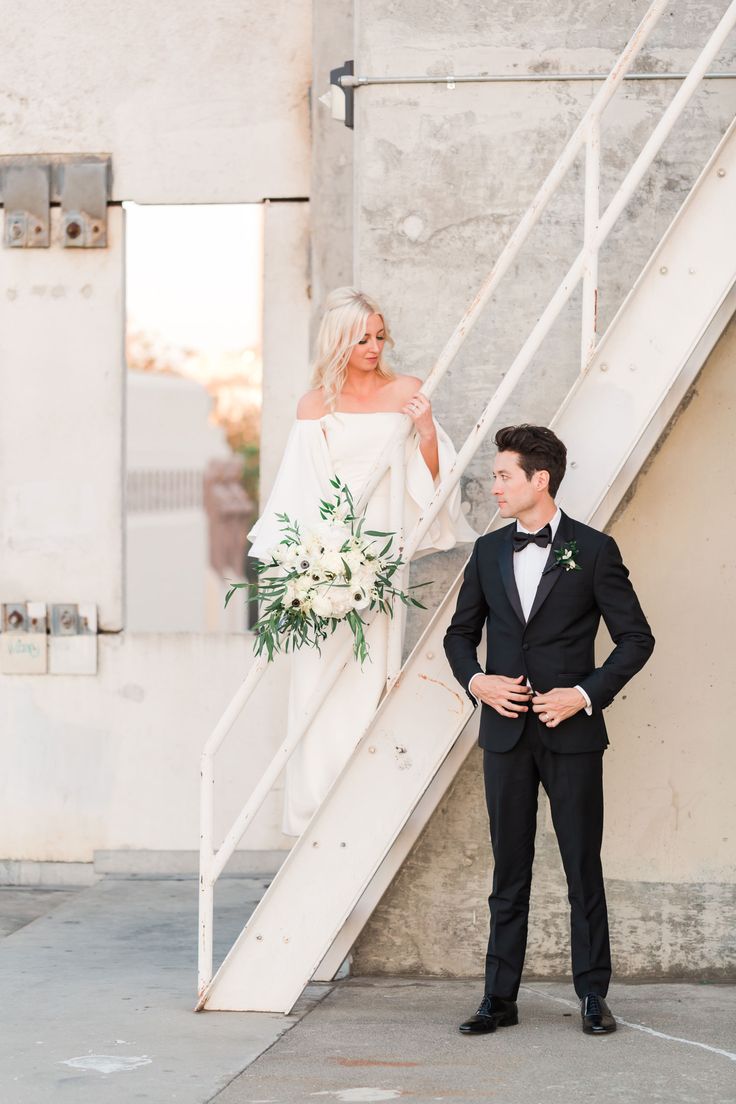 a bride and groom standing in front of a staircase